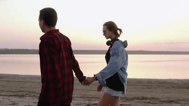 Sunset, sandy beach, a loving couple walks embraced on the deserted beach at sunset. Holding hands. Wearing in casual clothes - Footage, Video