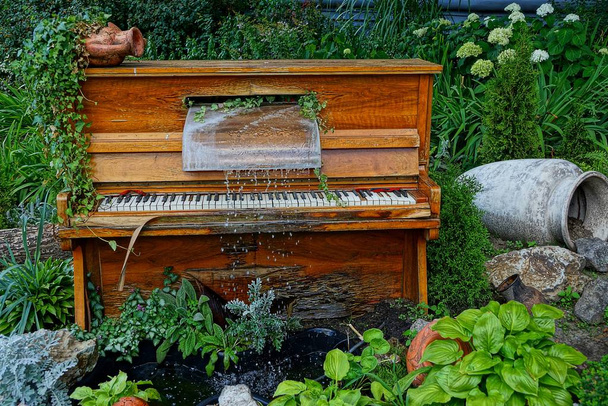 Старое пианино с ручьем воды среди зеленых растений
 - Фото, изображение
