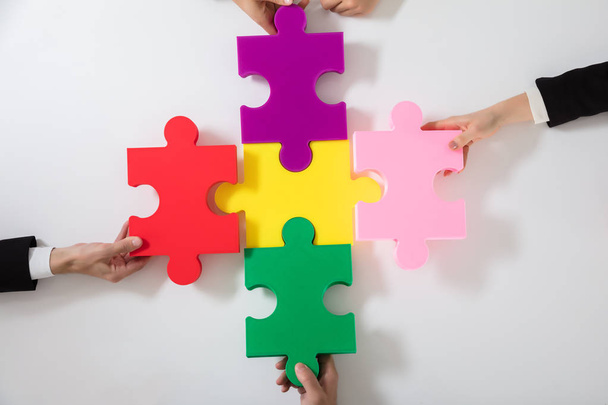 Group Of Businesspeople Solving Multi Colored Jigsaw Puzzle On Desk - 写真・画像