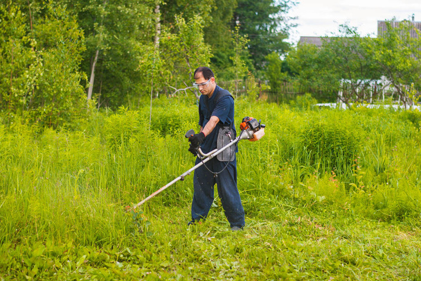 Человек с ручной газонокосилкой косит траву
 - Фото, изображение