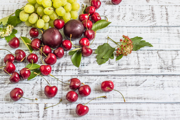 large sweet juicy cherries, plums and grapes, foliage and flowers on a wooden background, healthy eating concept - Foto, Imagen