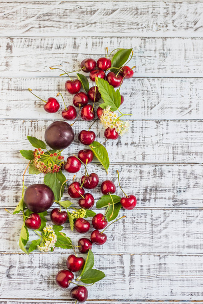 large sweet juicy cherries, plums and grapes, foliage and flowers on a wooden background, healthy eating concept - Foto, Imagen