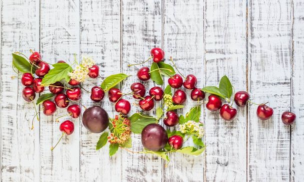 large sweet juicy cherries, plums and grapes, foliage and flowers on a wooden background, healthy eating concept - Фото, изображение