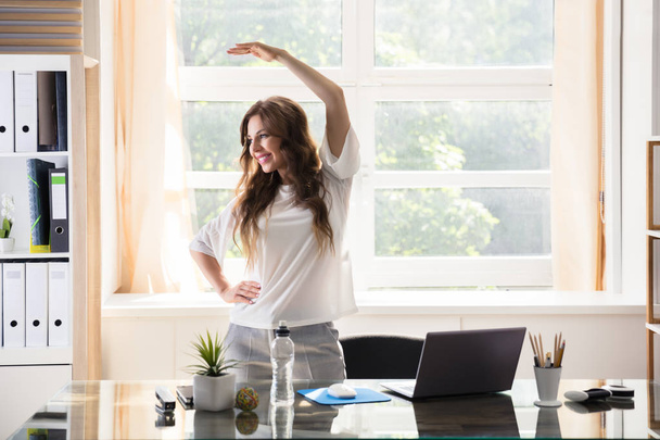 Happy Young Businesswoman Stretching Her Arms In Office - Foto, afbeelding