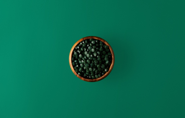 top view of wooden bowl with pile of spirulina pills isolated on green   - Φωτογραφία, εικόνα