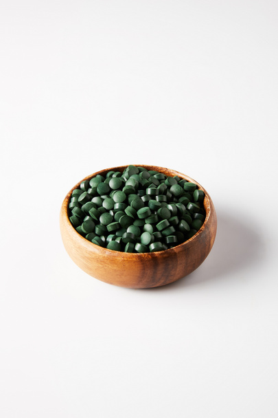 wooden bowl with pile of spirulina pills on grey background  - Photo, Image