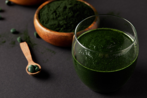 close up view of wooden spoon, glass of smoothie from spirulina, bowls with spirulina powder and spirulina pills on grey table  - 写真・画像