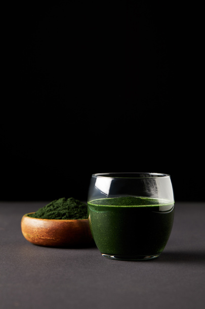 fresh spirulina drink in glass and spirulina powder in wooden bowl on black background  - Fotografie, Obrázek