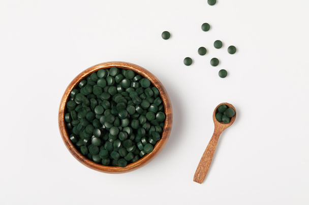 elevated view of wooden spoon and bowl with pile of spirulina pills on grey table  - Φωτογραφία, εικόνα