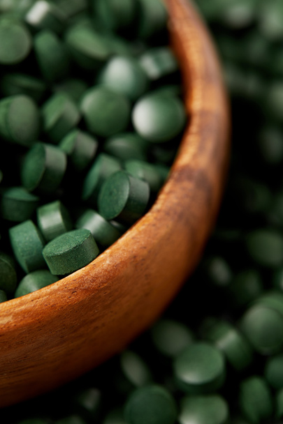 selective focus of wooden bowl with pile of spirulina pills  - Foto, afbeelding