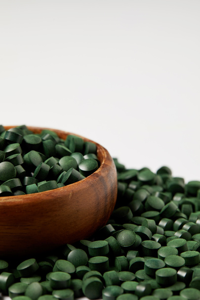 close up view of wooden bowl and pile of spirulina pills isolated on grey background  - Fotografie, Obrázek