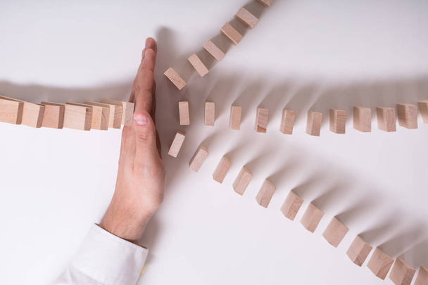 Close-up Of A Businessperson's Hand Stopping Wooden Blocks From Falling On White Background - Fotó, kép