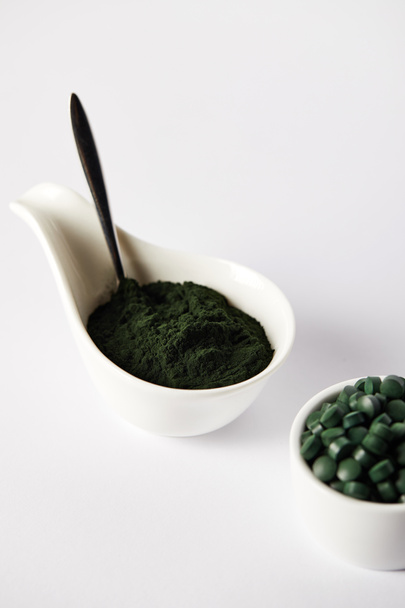 close up view of spoon, spirulina powder and spirulina pills in bowls on grey background  - Фото, зображення