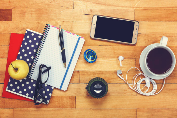 Cuadernos, bolígrafo, vasos, altavoces de música, auriculares, teléfono móvil, taza de té, manzana sobre un fondo de madera
. - Foto, Imagen