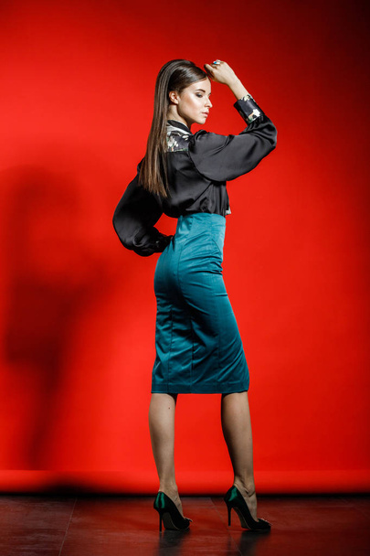 Studio portrait of young model in casual clothes on red background. Young woman in black shirt and blue skirt posing at studio  - Valokuva, kuva