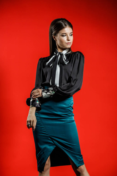 Studio portrait of young model in casual clothes on red background. Young woman in black shirt and blue skirt posing at studio  - Fotó, kép