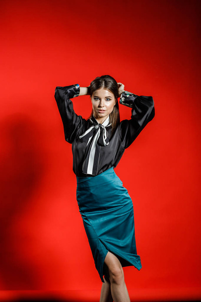 Studio portrait of young model in casual clothes on red background. Young woman in black shirt and blue skirt posing at studio  - Фото, зображення
