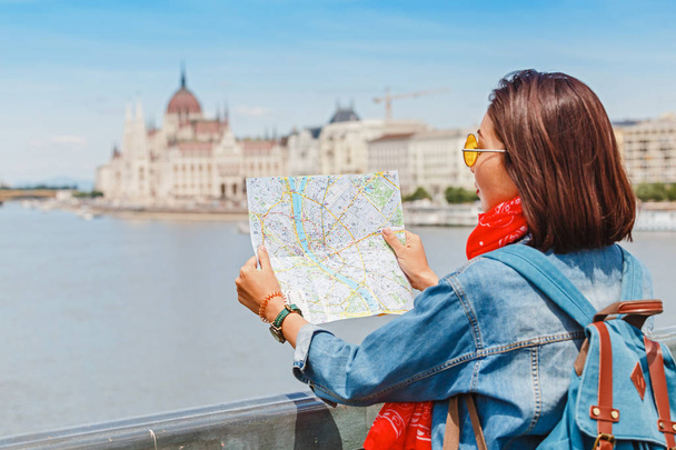 Feliz turista hipster asiático con mapa viaja en Budapest en el Parlamento húngaro en el fondo
 - Foto, Imagen