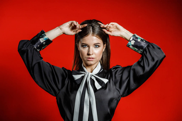 Closeup studio portrait of young model in casual clothes. Young woman with stylish haircut, wearing black shirt with bow on neck standing on red background  - Fotografie, Obrázek