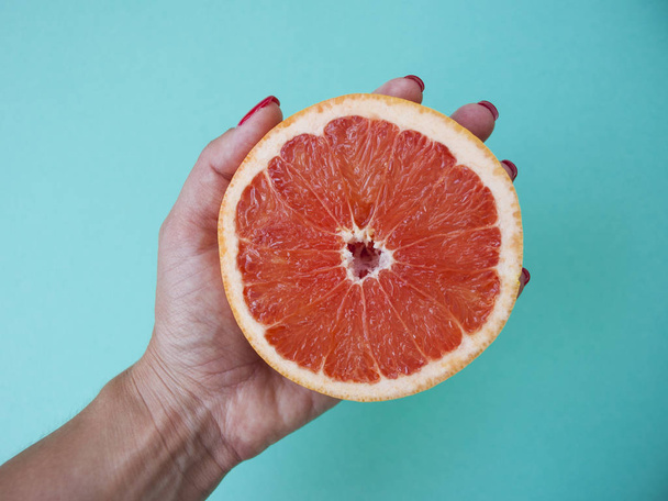 Lady's hand holding a beautiful juicy cut grapefruit on blue background. - Foto, imagen