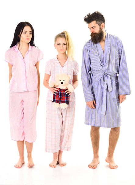 Man with beard, cute blonde and brunette girls with toy bear just wake up in morning. Sleepy morning concept. Girls with bearded macho in pajamas and robe in morning, isolated white background - Zdjęcie, obraz