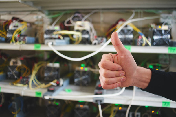 male hand showing thumbs up on background of farm equipment for mining cryptocurrency  - Photo, Image
