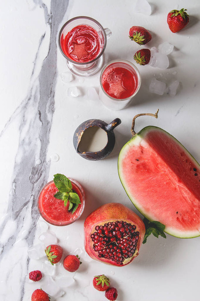 Three different red fruit berry watermelon, strawberry, raspberry, pomegranate cocktails or smoothies in glasses with crushed ice, fresh mint, ingredients above over white marble background. Flat lay - Foto, immagini