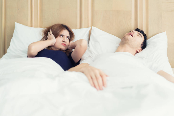 Annoyed Asian wife blocking her ears from noise of husband snoring in bedroom at home. Young couple have problem with man's snoring. - Foto, imagen
