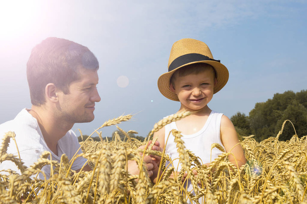 Happy family. Father and son on the wheat field. Male shows the boy ear of wheat. - Foto, imagen
