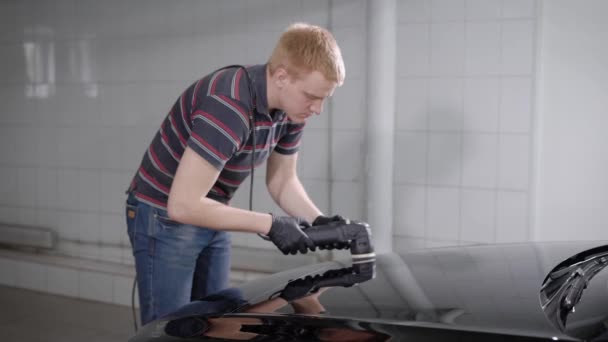 man van de jonge werknemer wordt verwerkt door auto oppervlak door elektrische polijst machine in een workshop - Video