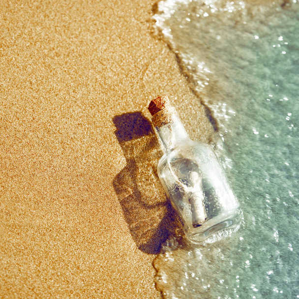 A bottle with a message is thrown by a wave on a sandy beach. Concept of hope The bottle floats in the surf line - 写真・画像