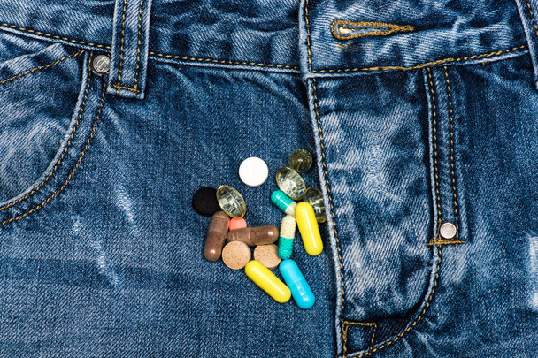 Pills or medicine tablets scattered on jeans near zip, denim background. Genitourinary problem concept. Zip of pants with colorful pills or capsules as symbol of disorders of genitourinary system - Zdjęcie, obraz