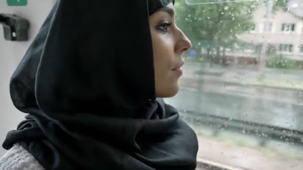 Mladá muslimka v hidžábu je sledovat v okně v trolejbusu, deštivé počasí. - Záběry, video