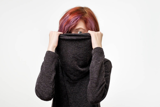Anonymous concept. Young woman with interesting colorful hairstyle hiding her face with colar. She does not want to be recognized. Protection of personal space - Photo, Image