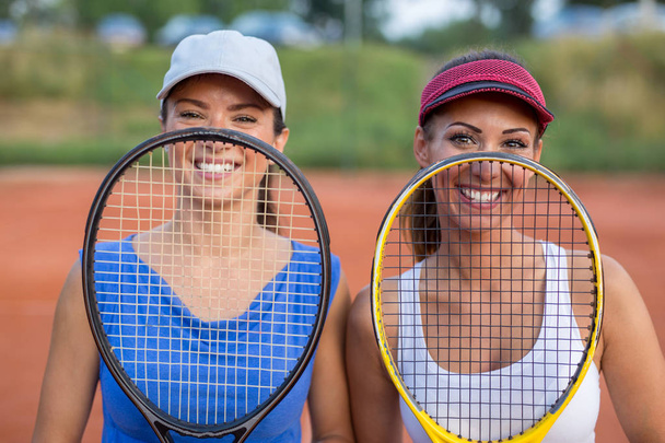 Two beautiful young women holding a tennis racket in front of their faces while smiling - Photo, Image