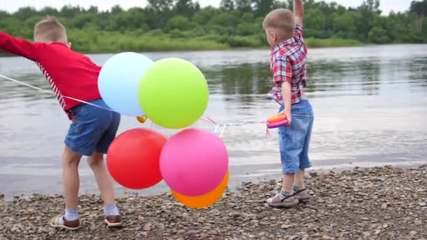 Due bambini giocano sulla riva del fiume. Lancia pietre, fai schizzi d'acqua. Bellissimo paesaggio estivo
. - Filmati, video
