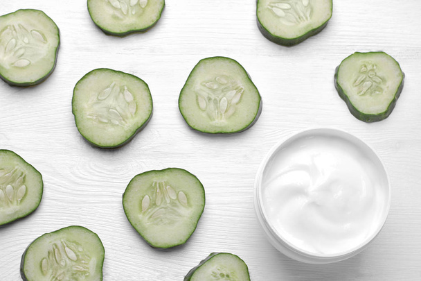 Face cream in a white jar with cucumber extract next to a set of fresh cucumbers on a white wooden background. Top view - Fotografie, Obrázek