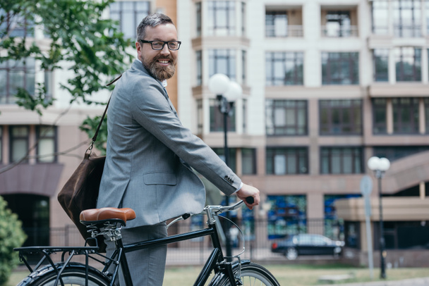 bearded handsome businessman standing with bike on street in city - Photo, Image