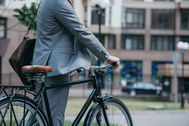 обрезанный образ бизнесмена, стоящего с велосипедом на улице в городе
 - Фото, изображение