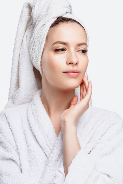 Young woman in a bathrobe and towel on her head, spa and care portrait, clean natural face, portrait on a white background isolated - Foto, afbeelding