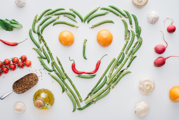 top view of heart made of fresh green peas and asparagus and smiley face from tomatoes and chili peppers isolated on white  - Photo, Image