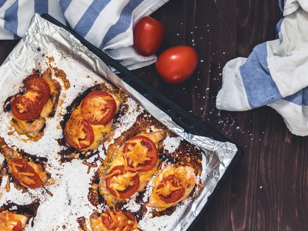 Chicken fillet baked with tomatoes and cheese on a baking sheet with foil. Delicious healthy food. Lifestyle. Flat lay. Top view. Wooden background - Valokuva, kuva