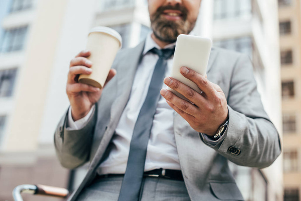 cropped view of businessman with coffee to go and smartphone - Foto, afbeelding