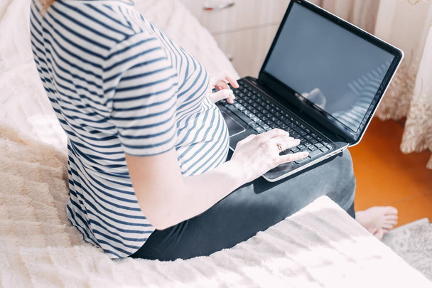 Pregnant woman working on laptop. Cropped image of pregnant businesswoman typing something on laptop while sitting at her working place at home - Foto, Bild