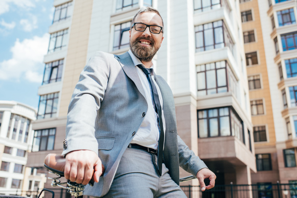 smiling businessman sitting on bicycle in city - Foto, Bild