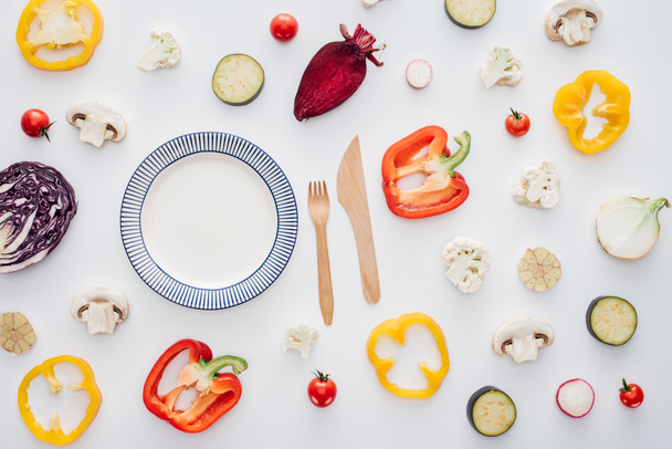 vista superior de la placa redonda vacía, tenedor de madera con cuchillo y verduras frescas en rodajas aisladas en blanco
 - Foto, Imagen
