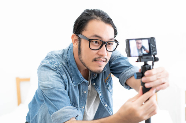 Jovem blogueiro asiático definindo câmera de vídeo com gravação de filmagens em casa
 - Foto, Imagem