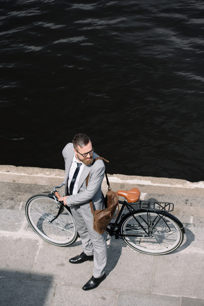 川の近くの岸壁に立っているバイクとひげを生やしたビジネスマンのオーバー ヘッド ビュー - 写真・画像