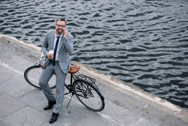 businessman with coffee to go talking on smartphone and standing with bike on quay - Foto, immagini