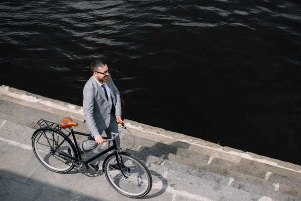 Blick aus der Vogelperspektive auf Geschäftsmann, der mit dem Fahrrad am Ufer des Flusses spaziert - Foto, Bild